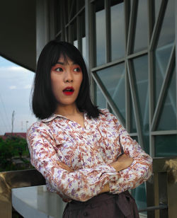 Portrait of young woman standing against window