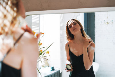 Young woman in black dress put day moisturizer body cream on clean fresh skin in bathroom at home