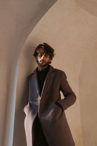 Portrait of young man with hands in pockets standing by wall