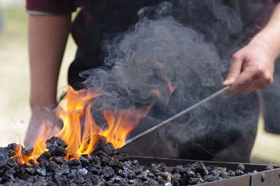 Midsection of man burning coal in barbecue