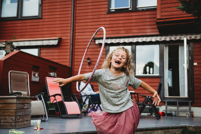 Cute girl having fun with hula hoop in backyard with red wooden house