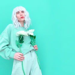 Portrait of woman holding flowers against blue background