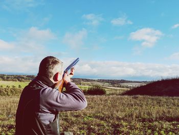 Man aiming rifle while standing against sky