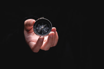 Close-up of hand holding navigational compass against black background