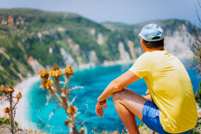 Rear view of man sitting on rock while looking at sea