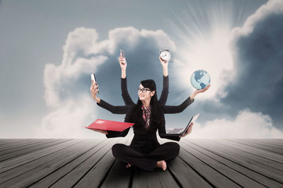 Full length of woman sitting with arms raised against sky