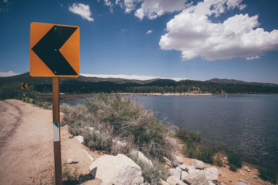 Road sign by lake against sky