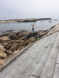 Man standing on rocks by sea against sky