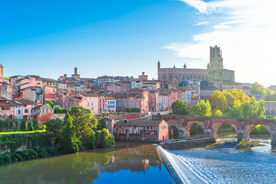 Arch bridge over river amidst buildings in city against sky