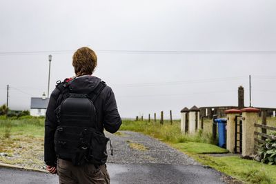 Rear view of man with backpack standing on land against sky