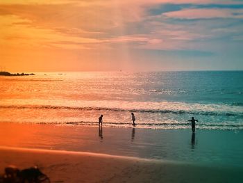 Silhouette people on beach against sky during sunset