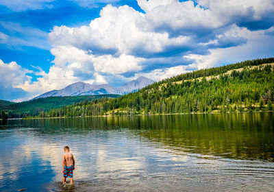 Rear view of shirtless boy in lake against forest