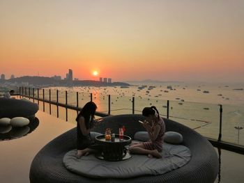 People on table by sea against sky during sunset