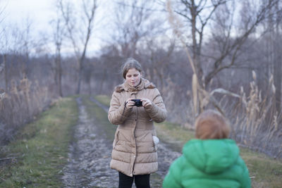 Mother photographing son while standing on field during winter