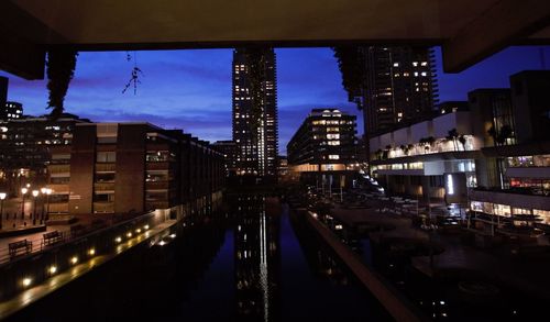 Illuminated street amidst buildings against sky at night