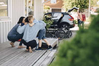 Mothers embracing son while gay couple standing by car during weekend