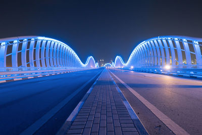 Illuminated bridge against blue sky at night