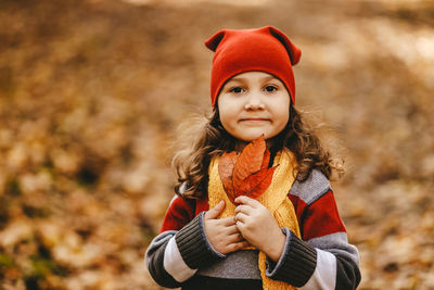 Portrait of a little girl a child in a warm hat walking holding an autumn leaf in the fall forest