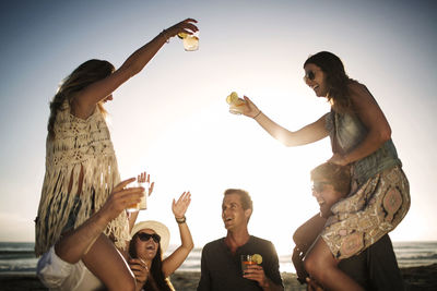 Cheerful men carrying female friends on shoulders while enjoying on beach