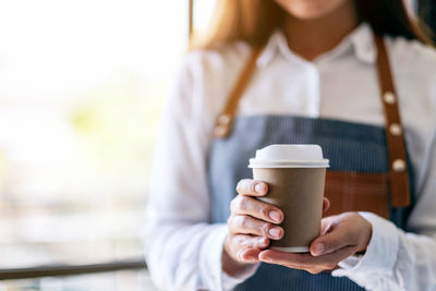 Midsection of woman holding disposable cup in cafe