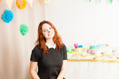 Portrait of smiling young woman standing against wall