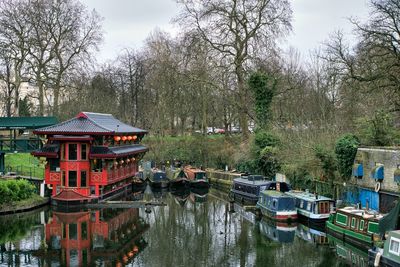 Boats moored in river by trees against sky