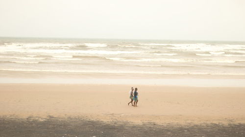 Couple walking on beach against sky