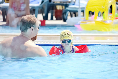 Rear view of man assisting daughter swimming in pool