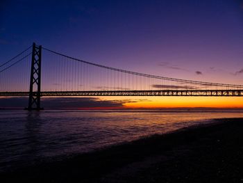 Suspension bridge over sea against sky at sunset