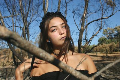 Portrait of young woman with bare tree against sky