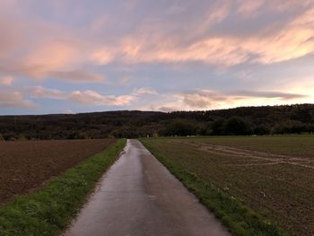 Empty road amidst field against sky during sunset