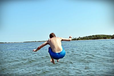 Rear view of shirtless man in sea against sky