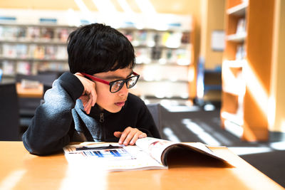 Boy reading book at table in library