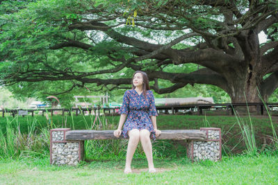 Portrait of woman sitting on bench against trees