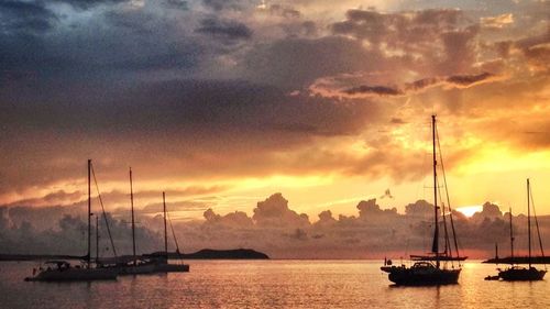 Sailboats moored on sea against sky during sunset