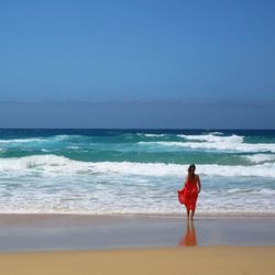 Rear view of woman standing at beach against clear sky