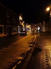 Illuminated street by buildings in city at night