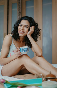Portrait of smiling young woman drinking coffee while sitting at home