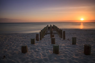 Wooden posts at sandy beach against sky during sunset