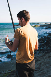 Rear view of man standing at beach against sky