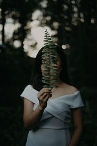 Woman holding plant in front of face during sunset