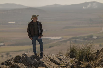 Portrait of adult man with cowboy hat standing on top of hill