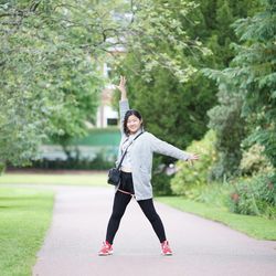 Portrait of happy young woman standing on footpath at park