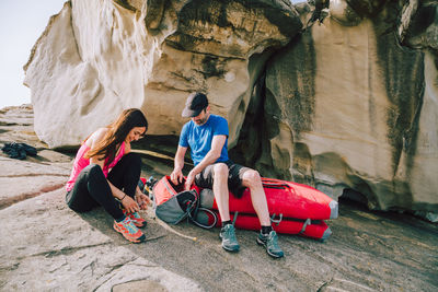 Full length of woman tying shoelace with man while sitting on rock