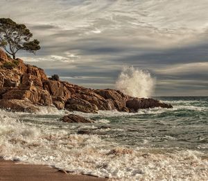 Waves splashing on rocks by sea against sky