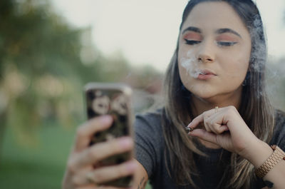 Young woman smoking cigarette using mobile phone