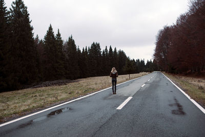 Man on road amidst trees against sky