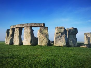 Circle of stones structure on field against blue sky