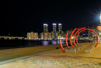 Illuminated buildings by river against sky at night