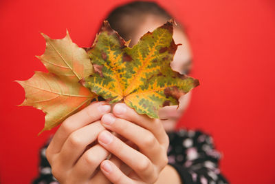 Close-up of girl holding dry leaves against wall